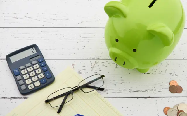 Calculator, reading glasses and a piggy bank on a desk